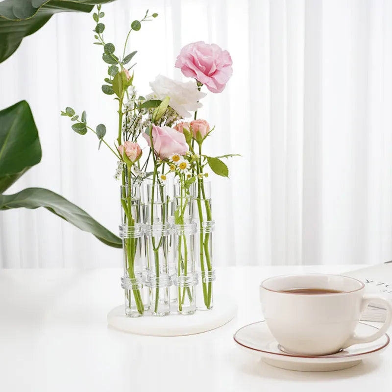 Clear hinged tube station holding flower stems on a tabletop; flowers are not included.